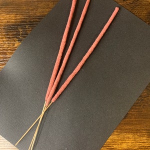 May include: Three brown incense sticks with a pink, fuzzy coating.