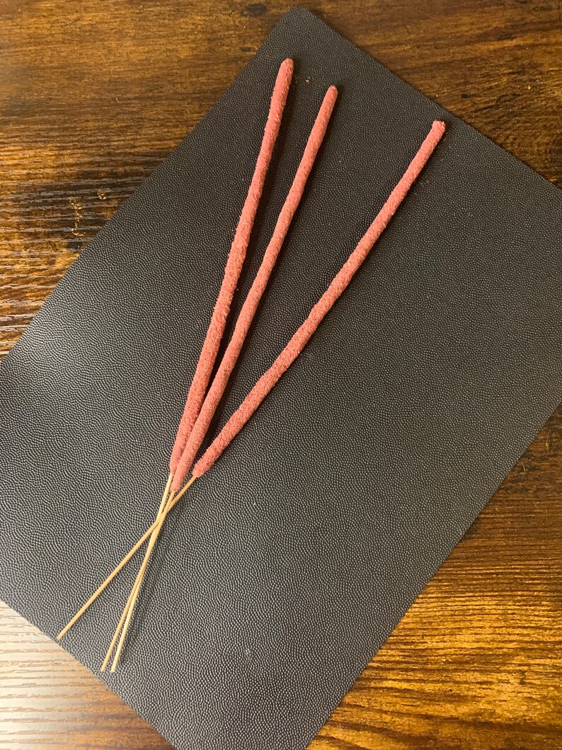 May include: Three brown incense sticks with a pink, fuzzy coating.