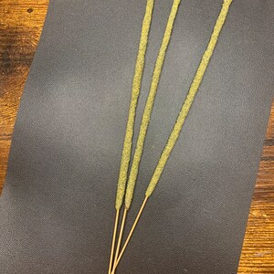 May include: Three green incense sticks with a brown wooden base on a black textured surface.