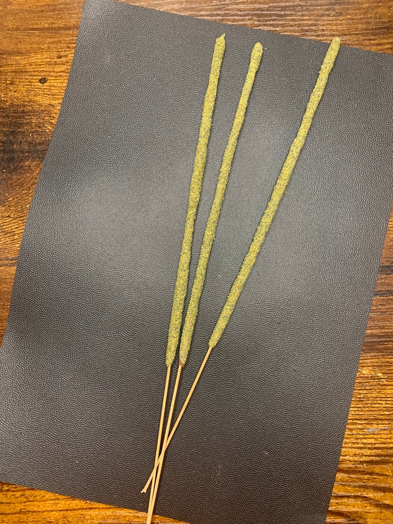 May include: Three green incense sticks with a brown wooden base on a black textured surface.