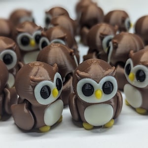 Peut inclure: Un groupe de figurines de hiboux brunes avec des ventres blancs et des yeux noirs. Les hiboux sont disposés en grappe sur une surface blanche.