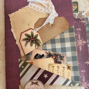 May include: A scrapbook page featuring a pocket with a burgundy herringbone background, a white lace ribbon, a brown paper tag with a holly illustration, and several vintage-style cards including one with the text Holly Jolly Christmas.