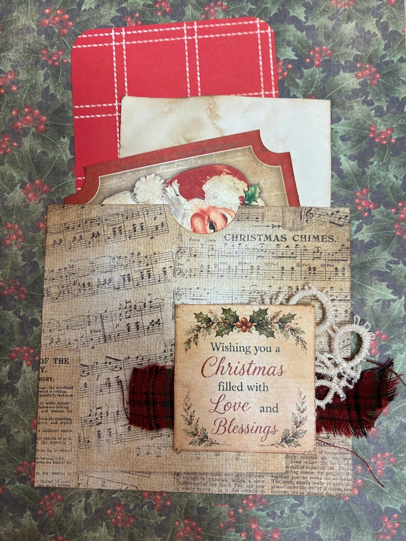 May include: A decorative paper pocket featuring vintage sheet music and the text Christmas Chimes. It holds a red plaid card, a cream-colored paper, and a Santa illustration. A square tag reads Wishing you a Christmas filled with Love and Blessings.
