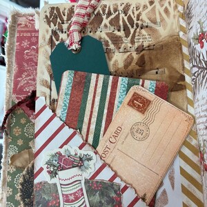 May include: A junk journal page featuring a vintage music sheet background, a dark green paper tag with a red and white striped ribbon, a striped card, and a postcard with a one-cent stamp. A die-cut Christmas stocking with holly is attached.