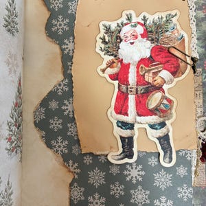 May include: A scrapbook page featuring a dark green background with white snowflake patterns. A piece of tan, burnt-edge paper is layered on top, holding a vintage-style cutout of Santa Claus carrying a sack, a drum, and a small gift.