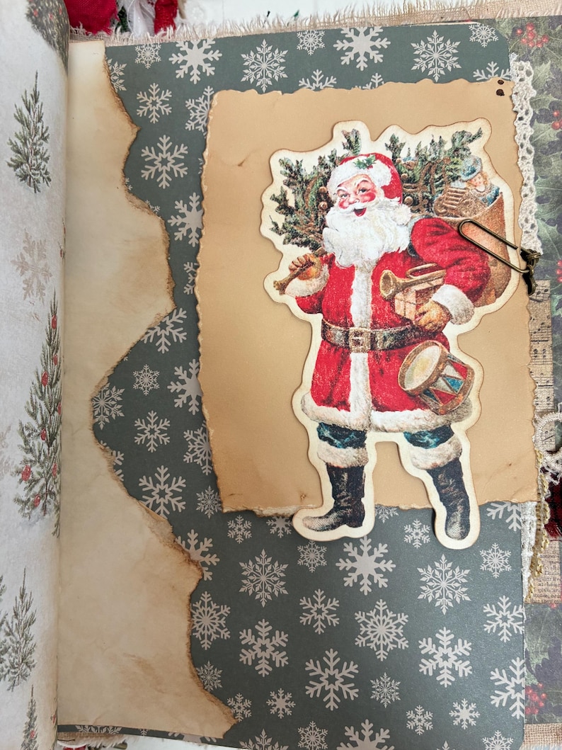 May include: A scrapbook page featuring a dark green background with white snowflake patterns. A piece of tan, burnt-edge paper is layered on top, holding a vintage-style cutout of Santa Claus carrying a sack, a drum, and a small gift.