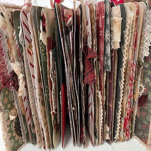 May include: A handmade junk journal featuring multiple pages with Christmas-themed patterns in red, green, and white. The book includes various paper textures, lace trim, fabric ribbons, and decorative elements like buttons and frayed edges.