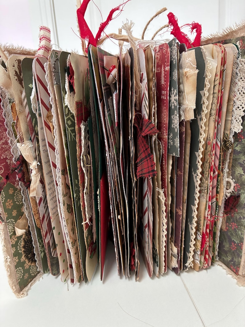 May include: A handmade junk journal featuring multiple pages with Christmas-themed patterns in red, green, and white. The book includes various paper textures, lace trim, fabric ribbons, and decorative elements like buttons and frayed edges.
