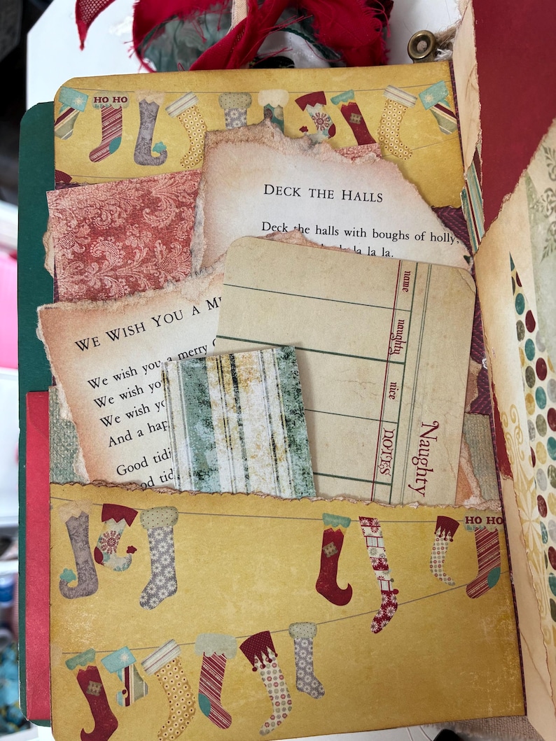 May include: A scrapbook page featuring a yellow background with a pattern of hanging Christmas stockings and the text HO HO. It includes torn paper inserts with the lyrics to Deck the Halls and We Wish You a Merry Christmas, plus a Naughty list card.