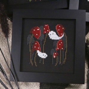 May include: A framed cross-stitch embroidery featuring a dark background with white ghosts and red mushrooms.