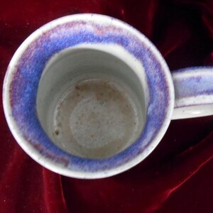 May include: A white ceramic mug with a blue and purple rim. The mug has a handle and is slightly dirty inside.