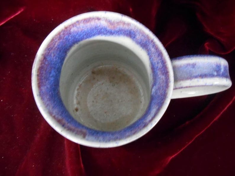 May include: A white ceramic mug with a blue and purple rim. The mug has a handle and is slightly dirty inside.