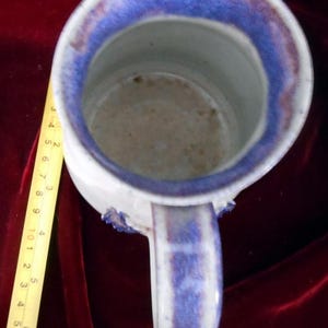 May include: A white ceramic mug with a blue and purple glaze. The mug has a handle and a wide rim.