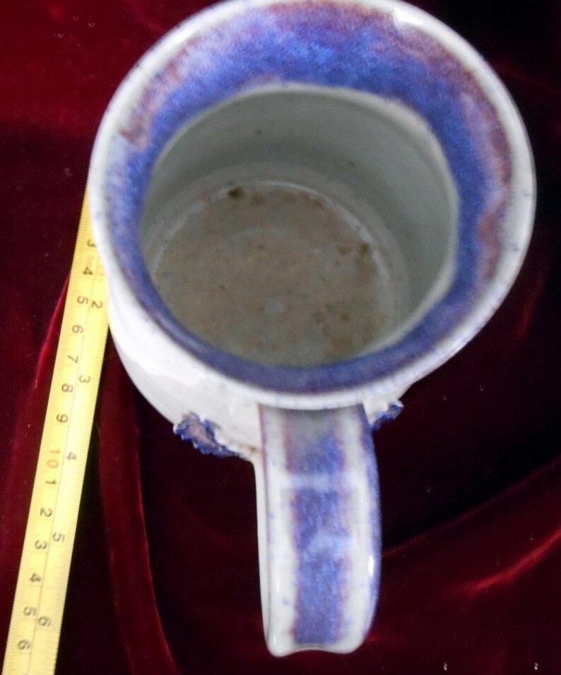 May include: A white ceramic mug with a blue and purple glaze. The mug has a handle and a wide rim.