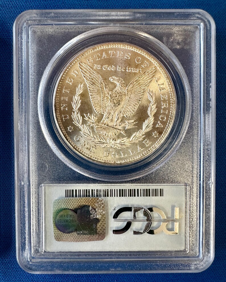 May include: A silver one-dollar coin in a clear plastic case. The coin shows an eagle with spread wings and the words "United States of America." The holder has a certification label with the letters "PCGS."