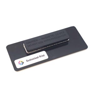 May include: A black name tag with a magnetic backing. The tag has the text "CAUTION - MAGNETIC DEVICE DO NOT USE WITH PACEMAKER" and a white sticker that says "Customised Print" with a colorful logo.