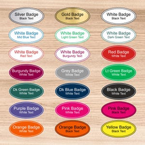 May include: A collection of twenty-one oval-shaped name badges in various colours including silver, gold, white, red, burgundy, grey, green, blue, black, purple, pink, orange, and yellow, each featuring printed text describing its specific colour.