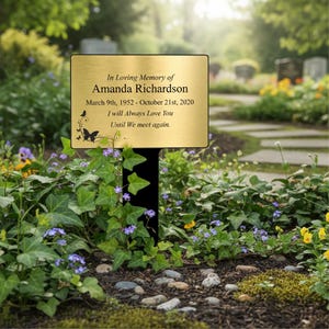 May include: A gold memorial plaque with the inscription "In Loving Memory of Amanda Richardson, March 9th, 1952 - October 21st, 2020. I will Always Love You Until We meet again." The plaque is set in a garden.