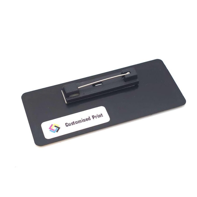 May include: A black rectangular name badge with a pin backing. The badge has a white sticker with the text "Customised Print" and a colorful logo. The pin is silver and the badge is made of a shiny black material.