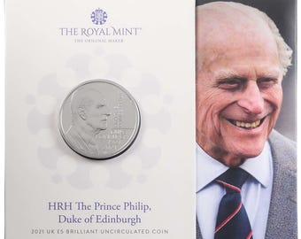 May include: A silver coin with a portrait of Prince Philip, Duke of Edinburgh, and the text "HRH The Prince Philip, Duke of Edinburgh 2021 UK ES Brilliant Uncirculated Coin" on the front. The coin is displayed in a white cardboard holder with a picture of Prince Philip on the back.