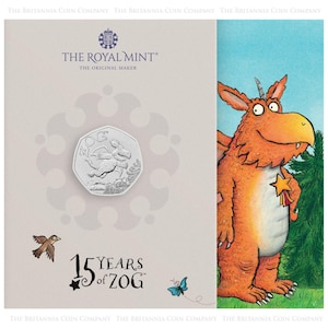 Peut inclure: Une pièce de monnaie commémorative argentée avec une illustration de Zog le dragon, avec le texte "15 Years of Zog". La pièce est placée sur un fond clair avec le logo Royal Mint. Une illustration colorée de Zog est à droite.