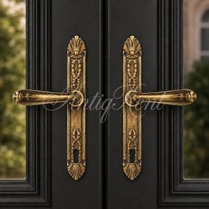May include: A pair of antique brass door handles with intricate floral and leaf engravings on long rectangular backplates. The handles feature a weathered gold finish and are mounted on a black door with a visible watermark reading Antig Kent.
