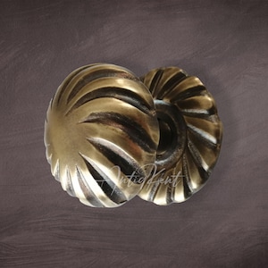 Può includere: Due pomelli per porte in ottone antico con un design decorativo a coste. I pomelli sono rotondi e hanno un centro leggermente rialzato.