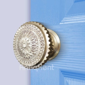 May include: A gold door knob with a detailed floral design. The knob is on a light blue door.