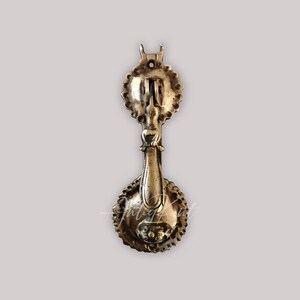 May include: Antique brass door knocker with a decorative design. The knocker has a round base and a long, ornate handle.