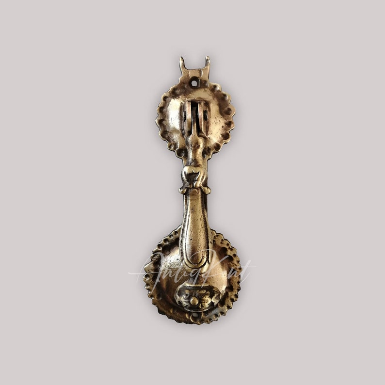 May include: Antique brass door knocker with a decorative design. The knocker has a round base and a long, ornate handle.
