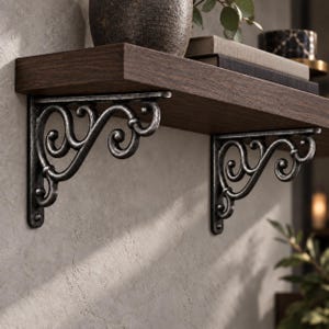 May include: Two dark silver-toned metal shelf brackets with an ornate, scrolled design featuring curved lines and loops. These brackets support a thick, dark brown wooden shelf board with a visible wood grain texture.
