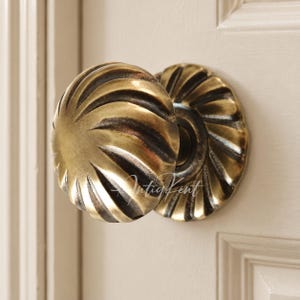 Könnte beinhalten: Ein runder Türknauf aus Messing mit einem wirbelnden, kannelierten Design und einer dunklen, gealterten Patina-Oberfläche. Der Knauf verfügt über eine passende kreisförmige Rosette mit demselben radialen Rillenmuster. Der Text IntiqKent ist sichtbar.