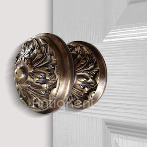 May include: A pair of ornate brass door knobs with a floral design. The knobs are round and have a raised, detailed pattern.