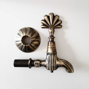 May include: Antique brass faucet with a decorative fan-shaped spout and a matching round base. The faucet has a vintage style and is perfect for a bathroom or kitchen.