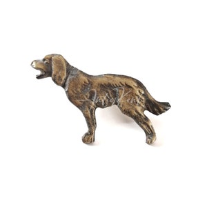 May include: A bronze-colored dog figurine in a standing pose with its mouth open. The dog has detailed features, including visible ears and a tail. The figurine is likely made of metal and is set against a white background.