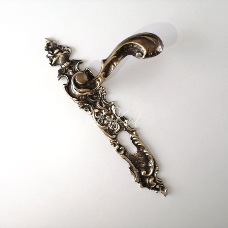 May include: Ornate brass door handle with a keyhole and intricate floral designs. The handle is in a vintage style and has a curved shape.