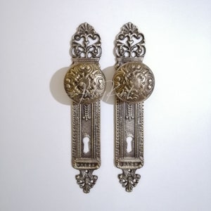 May include: A pair of antique-style door knobs with ornate metalwork and a keyhole. The knobs are brass in colour and have a decorative design.