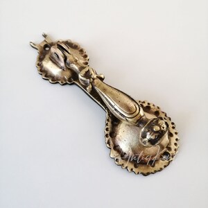 May include: Antique brass door knocker with a decorative design. The knocker has a rounded handle and a circular base with a raised design.