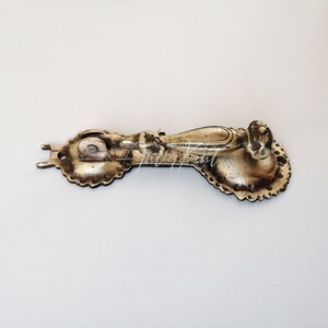 May include: A vintage brass door knocker with an ornate design. The knocker has a rounded handle and a decorative plate with a scalloped edge.