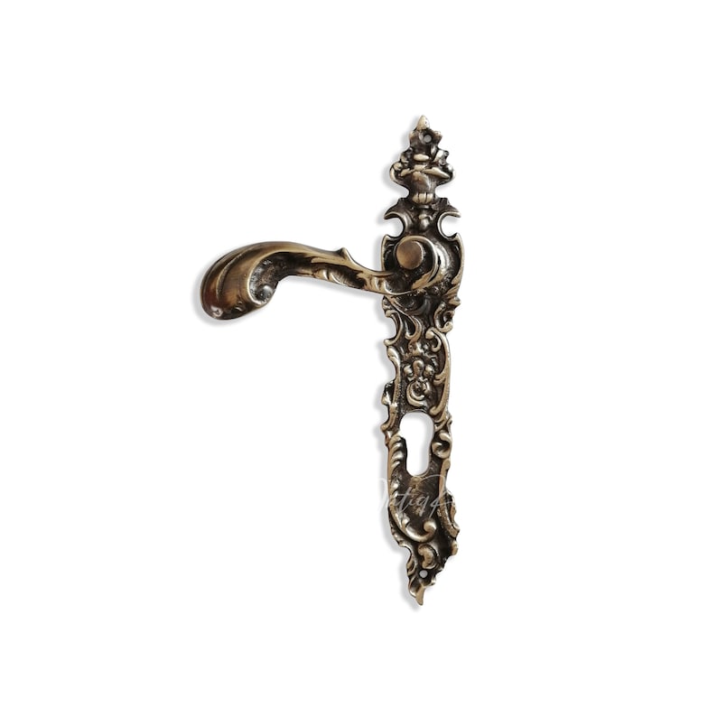 May include: Ornate brass door handle with a decorative, intricate design. The handle has a curved lever and a keyhole.