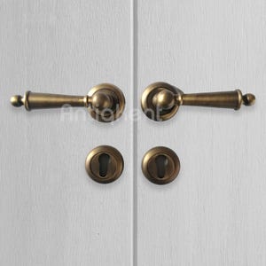 May include: A pair of antique brass door handles with keyholes. The handles have a rounded design and are attached to a white door.