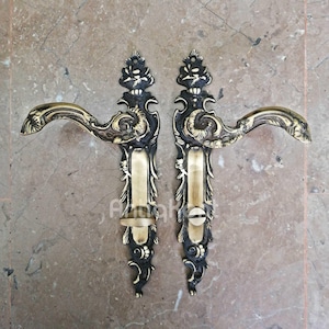 Könnte beinhalten: Zwei verzierte Messing-Türgriffe mit aufwendigen floralen Designs. Die Griffe sind im Vintage-Stil gehalten und haben eine schwarze Oberfläche.