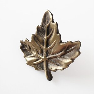 Op de afbeelding: Een gouden metalen esdoornblad met een gedetailleerd ontwerp. Het blad is een decoratief accent voor de inrichting van het huis.