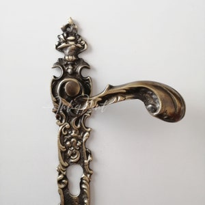 May include: Ornate brass door handle with a decorative, scroll-like design. The handle has a keyhole and a round knob.