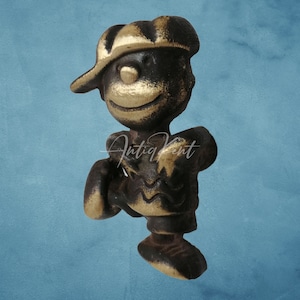 Peut inclure: Figurine en bronze d'un garçon souriant portant une casquette et une chemise à motifs. La figurine a une esthétique vintage, avec une finition vieillie. Le mot "AntiqKent" est écrit sur la figurine.
