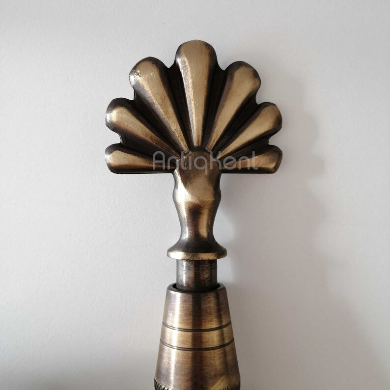 May include: A brass finial with a fan-shaped top and a round base. The finial is a decorative element often used on furniture, curtains, and other home decor items.