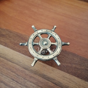 May include: Gold-toned metal ship wheel door knob with a detailed design. The knob has a round shape with spokes and a center hub.