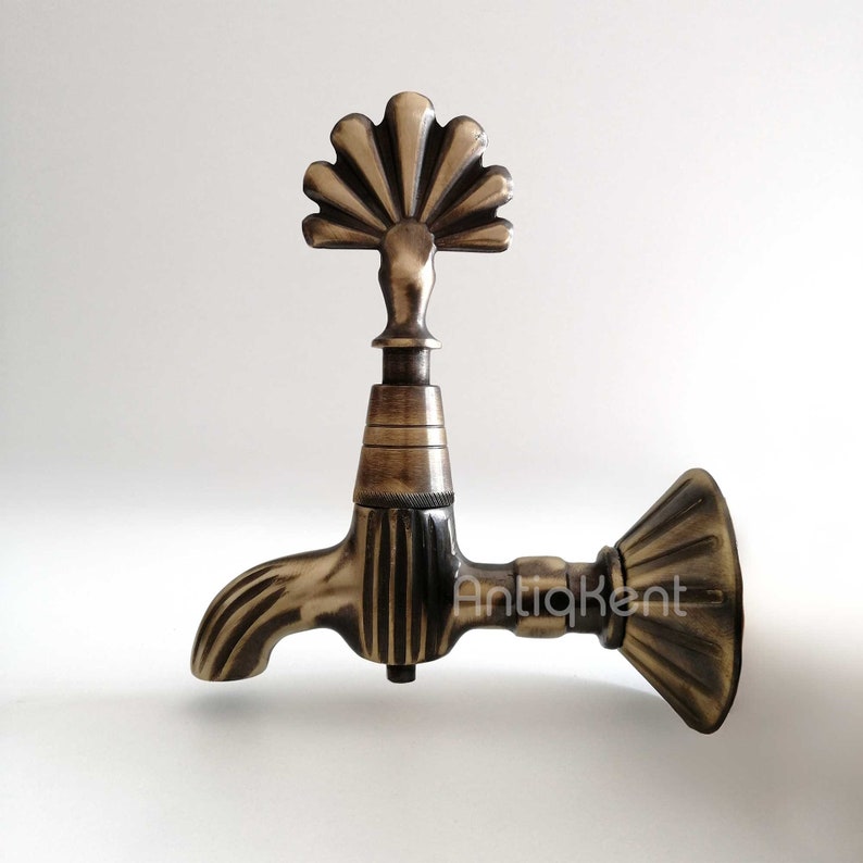 May include: Antique brass faucet with a decorative fan-shaped spout and a wall mount. The faucet has a vintage style and is made of solid brass.