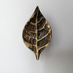 May include: A gold leaf-shaped decorative door knob or pull. The leaf has a detailed, textured surface.