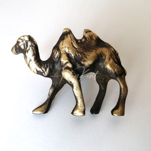 May include: A gold and black metal camel figurine. The camel is standing on all four legs with its head held high. The figurine is a decorative piece for the home.